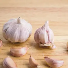 Dwie główki czosnku i kilka ząbków na drewnianym tle. Czosnek niedźwiedzi do czego? Do sałatek, sosów, pesto.