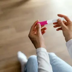 Dłonie trzymające test ciążowy, który może pomóc zidentyfikować objawy przed okresem.