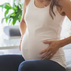 Kobieta w ciąży z dłońmi na brzuchu, zmartwiona. Może to być związane z brązowymi upławami w ciąży.