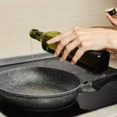 Ręka wylewa oliwę z oliwek do patelni, sprawdzając, czy oliwa z oliwek nadaje się do smażenia.