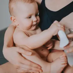 Mama z dzieckiem i laktatorem. Wiele mam zastanawia się, jak pobudzić laktację, a ten obrazek pokazuje jeden ze sposobów.