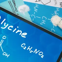 Tablet z napisem "Glycine" i wzorem chemicznym. Obok probówka z białym proszkiem. Dowiedz się, glicyna co to jest.