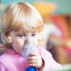 Mała dziewczynka z niebieskimi oczami robi inhalację na kaszel.