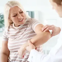 Lekarz bada ramię kobiety cierpiącej na bóle mięśni i stawów. Szuka domowych sposobów na ulgę.
