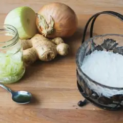 Cebula na przeziębienie: pokrojona cebula w słoiku, imbir, sól w ozdobnej miseczce i łyżeczka na drewnianym blacie.