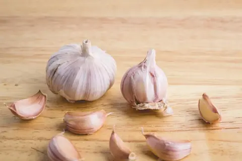 Dwie główki czosnku i kilka ząbków na drewnianym tle. Czosnek niedźwiedzi do czego? Do sałatek, sosów, pesto.