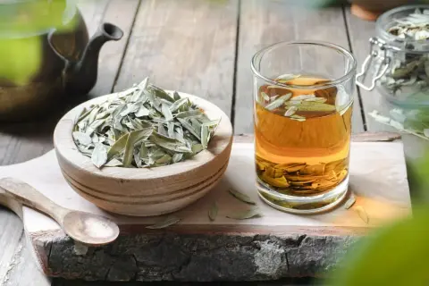 Napar z liści senesu w szklance, obok miseczka z suszem i drewniana łyżka. To naturalny sposób na zdrowie.