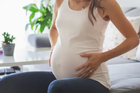 Kobieta w ciąży z dłońmi na brzuchu, zmartwiona. Może to być związane z brązowymi upławami w ciąży.