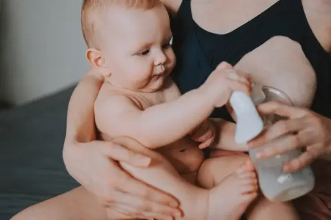 Mama z dzieckiem i laktatorem. Wiele mam zastanawia się, jak pobudzić laktację, a ten obrazek pokazuje jeden ze sposobów.