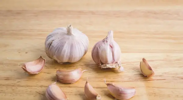 Dwie główki czosnku i kilka ząbków na drewnianym tle. Czosnek niedźwiedzi do czego? Do sałatek, sosów, pesto.