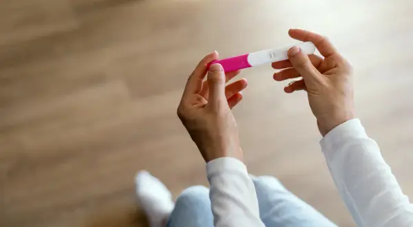 Dłonie trzymające test ciążowy, który może pomóc zidentyfikować objawy przed okresem.