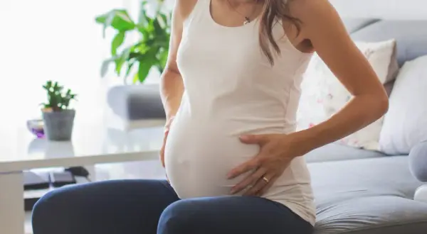 Kobieta w ciąży z dłońmi na brzuchu, zmartwiona. Może to być związane z brązowymi upławami w ciąży.