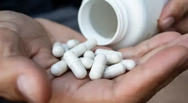 Garść białych kapsułek magnezu wysypana z białego opakowania. Jak przyjmować magnez? Zapytaj lekarza.