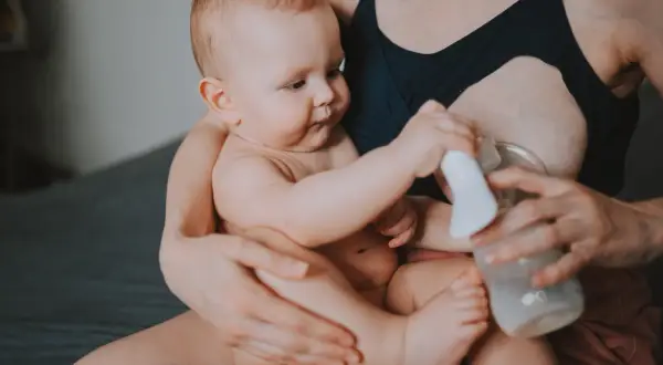 Mama z dzieckiem i laktatorem. Wiele mam zastanawia się, jak pobudzić laktację, a ten obrazek pokazuje jeden ze sposobów.
