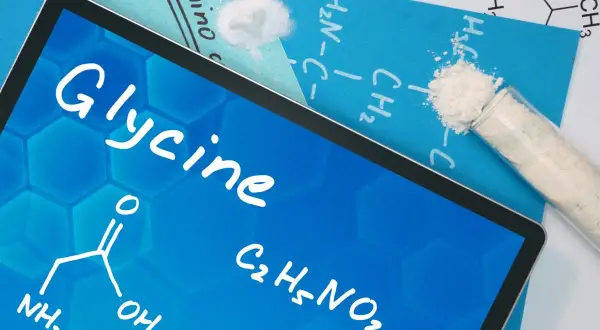 Tablet z napisem "Glycine" i wzorem chemicznym. Obok probówka z białym proszkiem. Dowiedz się, glicyna co to jest.