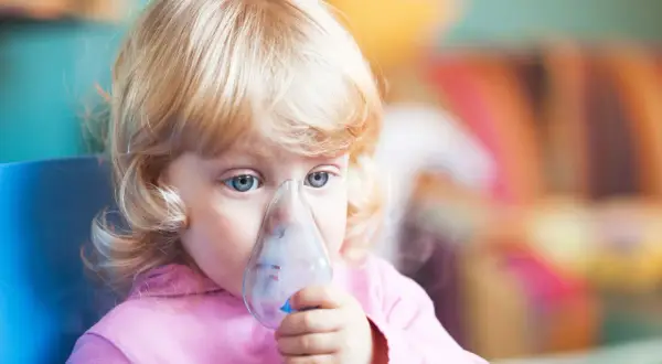 Mała dziewczynka z niebieskimi oczami robi inhalację na kaszel.