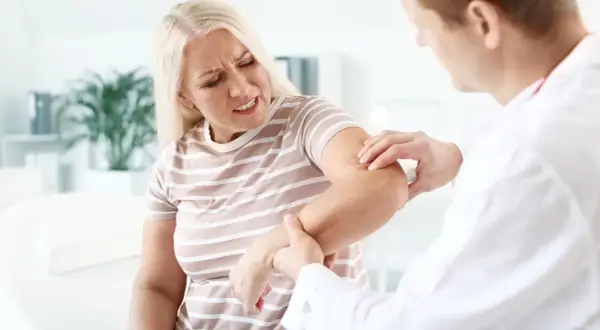 Lekarz bada ramię kobiety cierpiącej na bóle mięśni i stawów. Szuka domowych sposobów na ulgę.