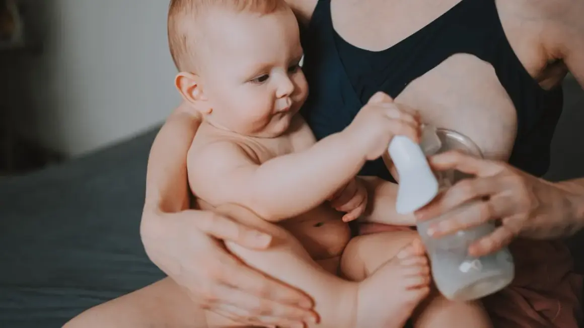 Mama z dzieckiem i laktatorem. Wiele mam zastanawia się, jak pobudzić laktację, a ten obrazek pokazuje jeden ze sposobów.
