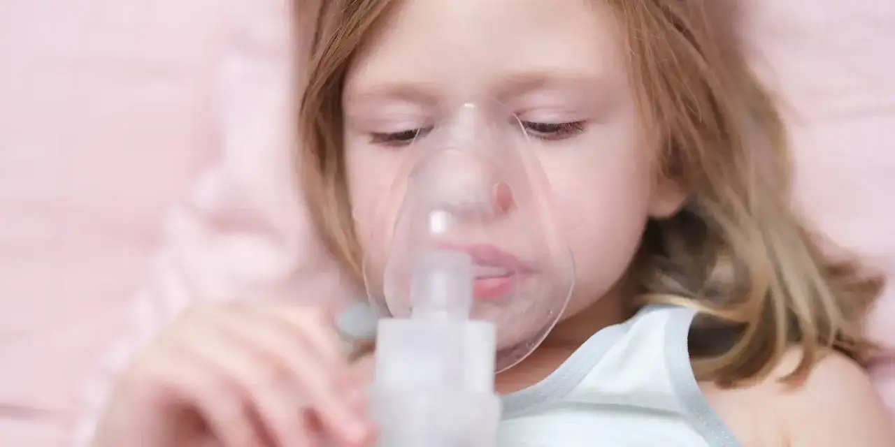 Mała dziewczynka z maską inhalacyjną na twarzy. Inhalacja na kaszel pomaga jej oddychać.