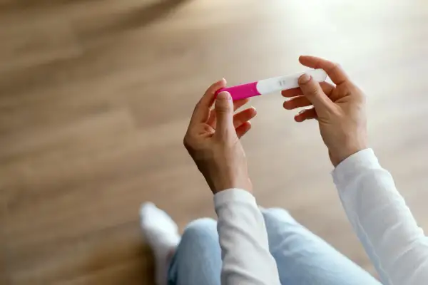 Dłonie trzymające test ciążowy, który może pomóc zidentyfikować objawy przed okresem.