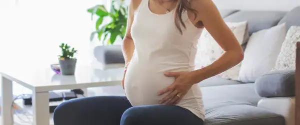 Kobieta w ciąży z dłońmi na brzuchu, zmartwiona. Może to być związane z brązowymi upławami w ciąży.