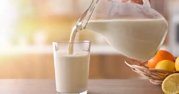 Mleko bez laktozy nalewane do szklanki. Czy mleko bez laktozy jest zdrowe? W koszyku owoce: pomarańcze i cytryny.