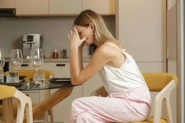 Kobieta siedzi przy stole, z rękami na twarzy, odczuwając senność po jedzeniu.