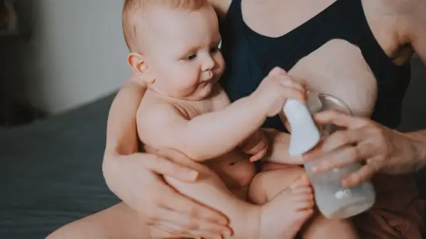 Mama z dzieckiem i laktatorem. Wiele mam zastanawia się, jak pobudzić laktację, a ten obrazek pokazuje jeden ze sposobów.