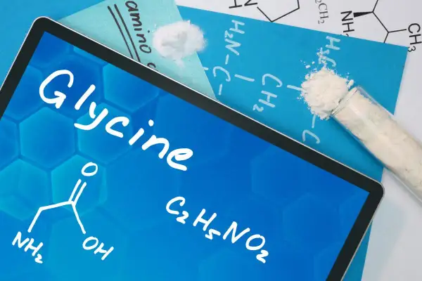 Tablet z napisem "Glycine" i wzorem chemicznym. Obok probówka z białym proszkiem. Dowiedz się, glicyna co to jest.
